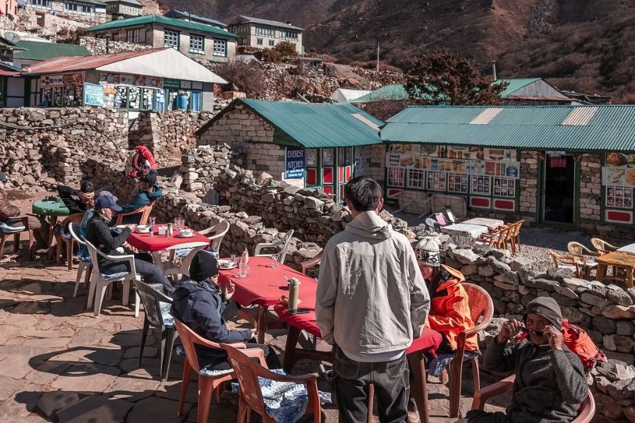 Trekkers dining at outdoor tables beside stone teahouse with green roof